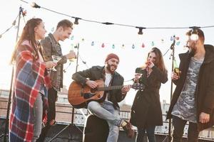 alle sind glücklich. fünf junge Freunde feiern mit Bier und Gitarre auf dem Dach foto