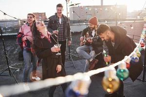 lautes Lachen. Glühbirnen überall auf dem Dach, wo eine junge Gruppe von Freunden beschlossen hat, ihr Wochenende mit Gitarre und Alkohol zu verbringen? foto