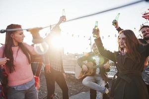 tanzen bei Sonnenschein. Gruppe junger Leute, die auf einem Dach mit etwas Alkohol und Gitarrenspiel feiern?