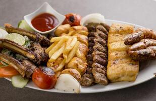 persisch mischen Grill Teller mit Tikka boti, Lamm hacken, Fleisch Kebab, Fisch, Fritten und Tomate Soße serviert im Gericht isoliert auf grau Hintergrund oben Aussicht von Arabisch Essen foto