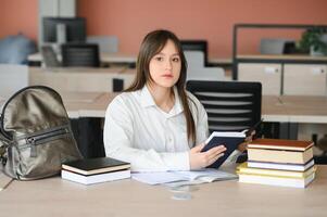 ein süß 15-jährige Schülerin sitzt beim ein Schule Schreibtisch mit Notizbücher und Bücher und Studien foto