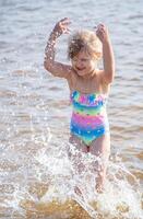 jung glücklich Kind Mädchen von europäisch Aussehen Alter von 6 haben Spaß im Wasser auf das Strand und Spritzwasser, tropisch Sommer- Berufe,Ferien.a Kind genießt das Meer.vertikal Foto. foto