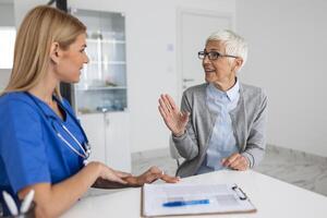 jung Frau Arzt oder gp im Weiß medizinisch Uniform konsultieren Senior weiblich geduldig im Privat Krankenhaus. weiblich Therapeut sprechen sich unterhalten mit Frau Klient auf Beratung im Klinik. foto