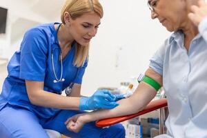 Vorbereitung zum Blut Prüfung mit Senior Frau durch weiblich Arzt medizinisch Uniform auf das Tabelle im Weiß hell Zimmer. Krankenschwester durchbohrt das Patienten Arm Vene mit Nadel leer Rohr. foto