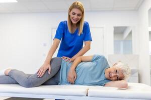 jung Arzt Chiropraktiker oder Osteopath Festsetzung Lügen Senior Frau zurück mit Hände Bewegungen während Besuch im Handbuch Therapie Klinik. Fachmann Chiropraktiker während Arbeit foto