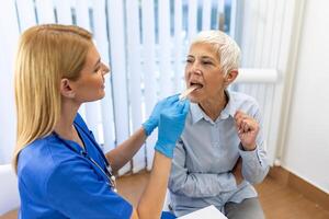 Senior geduldig Öffnung ihr Mund zum das Arzt zu aussehen im ihr Kehle. weiblich Arzt Prüfung wund Kehle von geduldig im Klinik. HNO-Arzt untersucht wund Kehle von geduldig. foto