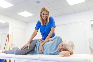 Fachmann Chiropraktiker oder Physiotherapeut hilft zu heilen ein Senior Frau zurück. Arzt behebt das geduldig Lügen auf ein Couch von ein modern Rehabilitation Klinik Konzept von physisch Rehabilitation. foto