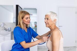 Pflege weiblich Arzt verwenden Phonendoskop untersuchen Senior geduldig Herz Bewertung beim Beratung im Krankenhaus. Frau Krankenschwester oder gp verwenden Stethoskop Hör mal zu zu Frau Herzschlag im Klinik. foto