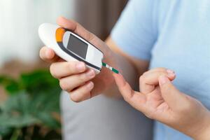 asiatisch Frau mit Lanzette auf Finger zum Überprüfung Blut Zucker Niveau durch Glucose Meter, Diabetes. foto