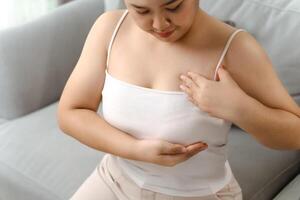 asiatisch Frau Überprüfung Klumpen auf ihr Brust zum Zeichen von Brust Krebs durch ihr selbst beim heim. foto