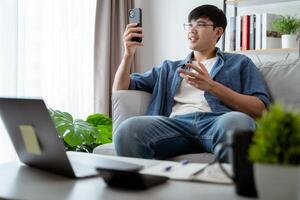 ein Mann ist Sitzung auf ein Couch und suchen beim seine Zelle Telefon foto