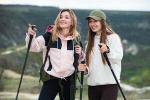 zwei jung Frauen freunde Wanderer mit Rucksäcke und Trekking Stangen auf oben von ein Berg. reisen, Reisender. foto