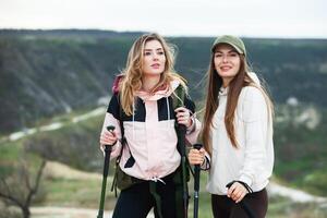 zwei jung Frauen freunde Wanderer mit Rucksäcke und Trekking Stangen auf oben von ein Berg. reisen, Reisender. foto