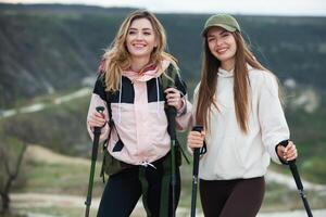 zwei jung Frauen freunde Wanderer mit Rucksäcke und Trekking Stangen auf oben von ein Berg. reisen, Reisender. foto