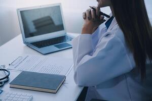 Arzt und geduldig Sitzung beim das Schreibtisch im Klinik Büro. das Fokus ist auf weiblich Arzt Hände Füllung oben das Medikation Geschichte Aufzeichnung form, schließen hoch. Medizin Konzept foto