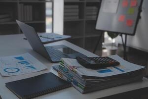 schließen oben Aussicht von einfach Arbeitsplatz mit Laptop, Notizbücher, Kaffee Tasse und Baum Topf auf Weiß Tabelle mit verschwommen Büro Zimmer Hintergrund foto