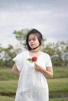 Porträt von ein ziemlich jung Frau gekleidet im Weiß Kleid halten Rose Blumen foto