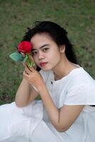 Porträt von ein ziemlich jung Frau gekleidet im Weiß Kleid halten Rose Blumen foto
