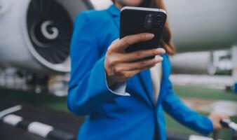 jung asiatisch Frau im International Flughafen, mit Handy, Mobiltelefon Smartphone und Überprüfung Flug beim das Flug Information Tafel foto