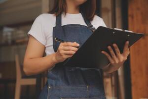 Startup erfolgreicher Kleinunternehmer SME Schönheitsmädchen steht mit Tablet-Smartphone im Café-Restaurant. Porträt der Barista-Café-Besitzerin mit asiatischer Bräune. KMU-Unternehmer-Verkäufer-Geschäftskonzept foto