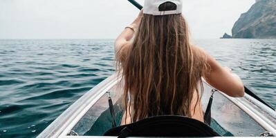 Frau im Kajak zurück Sicht. glücklich jung Frau mit lange Haar schwebend im transparent Kajak auf das Kristall klar Meer. Sommer- Urlaub Ferien und heiter weiblich Menschen entspannend haben Spaß auf das Boot foto