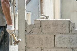 Hand von Arbeiter mit Hammer zerschlagen und zerstören auf Backstein Mauer beim Konstruktion Seite? ˅ foto