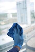 Hand im Blau Handschuh Reinigung Fenster mit Grün Lappen foto