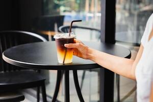 Frau Trinken vereist Kaffee im wegbringen Plastik Tasse beim Tabelle draussen Cafe. foto