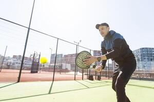 ein Padel Spieler springen zu das Ball, gut suchen zum Beiträge und Poster. Mann mit schwarz Schläger spielen ein Spiel im das öffnen hinter das Netz Gericht draußen. Fachmann Sport Konzept mit Raum zum Text foto