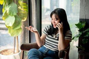 ein positiv asiatisch Frau ist reden auf das Telefon mit jemand während Sitzung im ein Kaffee Geschäft. foto