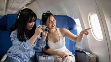 zwei heiter jung asiatisch weiblich freunde sind genießen reden und nehmen Bilder während das Flug. foto