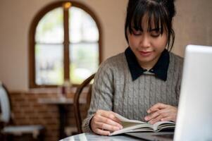 ein konzentriert jung asiatisch weiblich Hochschule Schüler ist lesen ein Lehrbuch während Sitzung im ein Cafe. foto