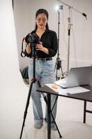 ein Fachmann asiatisch weiblich Fotograf ist einstellen ihr dslr Kamera auf ein Stativ Stand. foto