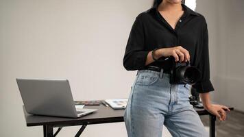 ein abgeschnitten Schuss von ein weiblich Fotograf ist Stehen im ihr Studio mit ein dslr Kamera im ihr Hand. foto