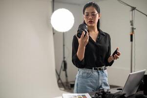 Fachmann asiatisch weiblich Fotograf ist vorbereiten ihr Kamera zum ein Foto-Shooting, Arbeiten im ein Studio foto