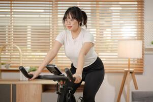 ein stark asiatisch Frau im Sportbekleidung ist ausüben auf ein Fitness Fahrrad, tun Innen- Cardio beim heim. foto