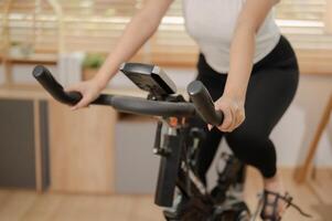 ein abgeschnitten Bild von ein Frau im Sportbekleidung ausüben auf ein Fitness Fahrrad, tun Innen- Cardio beim heim. foto