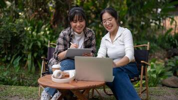 zwei asiatisch weiblich sind reden und Arbeiten auf ein Projekt zusammen während Sitzung beim ein draussen Tisch. foto