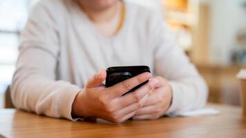 ein abgeschnitten Schuss von ein asiatisch Frau mit ihr Smartphone beim ein Tabelle im ein gemütlich Kaffee Geschäft. foto