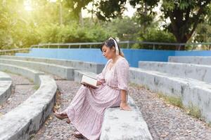 Frau tragen Kleid lesen ein Buch im ein Park. foto