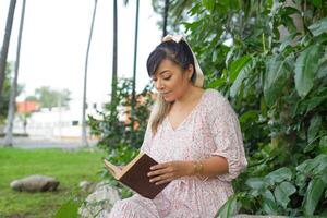 Frau sitzend Nächster zu ein Baum Kofferraum im ein Park lesen ein Buch. Welt Buch Tag. Konzept von Lektüre. foto