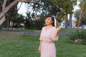 Frau mit positiv Einstellung tragen Kleid und Bogen im ihr Haar im ein Öffentlichkeit Park nehmen ein gehen. foto