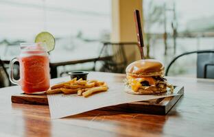 köstlich Hamburger mit Fritten und Erdbeere Cocktail serviert auf ein hölzern Tisch. Hamburger mit Erdbeere Cocktail serviert auf Tabelle foto