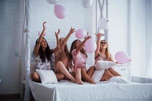 wie Kinder auf der Party. auf dem weißen Luxusbett mit Luftballons und Hasenohren sitzen. Vorstellung von Bachelorette foto