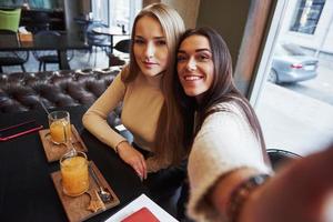 Foto vom Handy des Mädchens. Junge Freundinnen machen Selfie im Restaurant mit zwei gelben Getränken auf dem Tisch