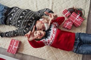 Hände in die Luft. Draufsicht des Paares in Weihnachtskleidung liegt auf dem Boden mit Geschenken darauf