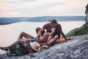 zum Kuss hinlegen. junges Paar hat beschlossen, seinen Urlaub aktiv am Rande des wunderschönen Felsens mit See im Hintergrund zu verbringen foto