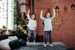 Hände hoch. Foto der Bewegung. fröhliche Kinder, die Spaß haben und auf dem Bett mit dekorativem Feiertagshintergrund springen