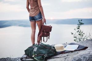 Einsames Mädchen, das in der Nähe des Randes des Felsens steht und eine schöne Landschaft mit einer Tasche in den Händen beobachtet foto