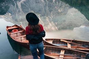 Spiegelungen im Wasser sehen aus wie echte. Frau mit schwarzem Hut genießt majestätische Berglandschaft in der Nähe des Sees mit Booten foto